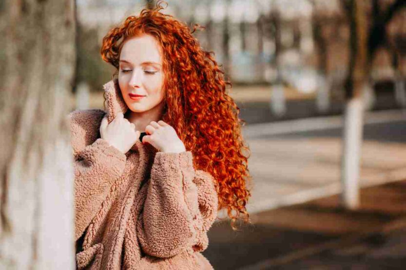 Primo piano di ragazza dai capelli rossi ricci con cappotto alla moda marrone